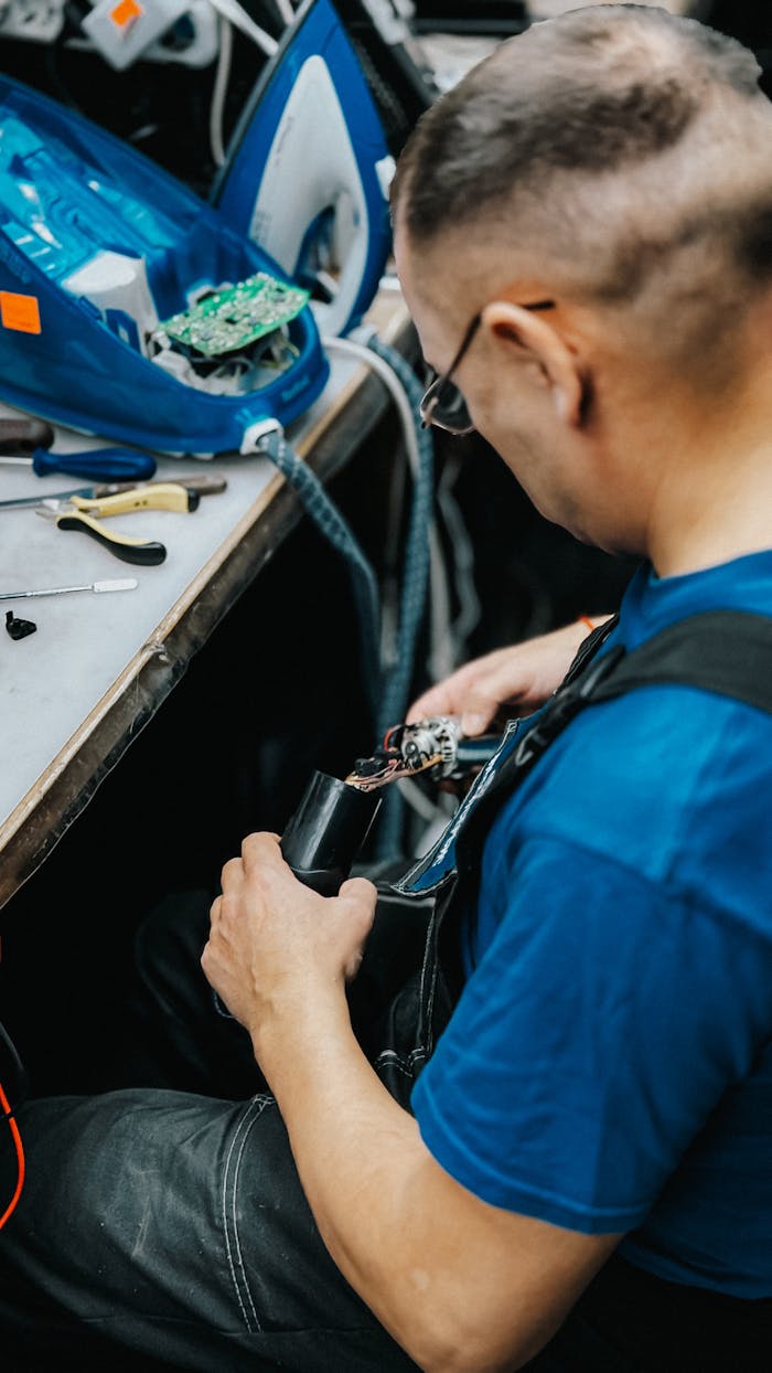 A skilled technician repairs an electronic device indoors, focused on intricate wiring and components.